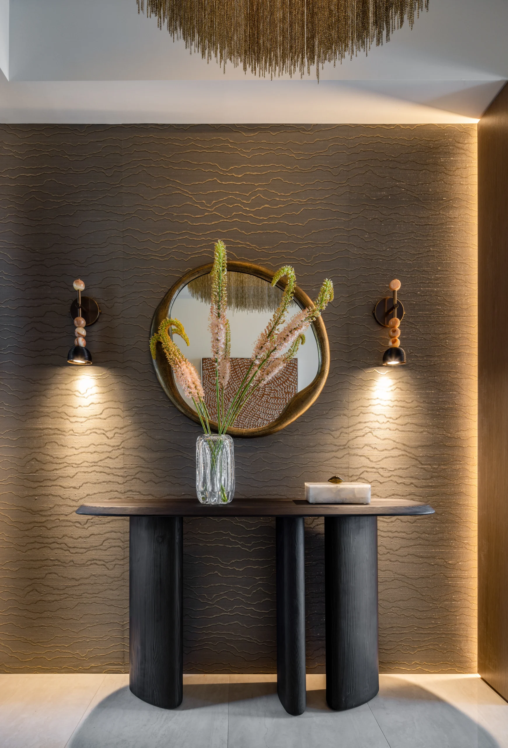 Sculptural entry console with textured wall finish, round mirror and warm accent lighting