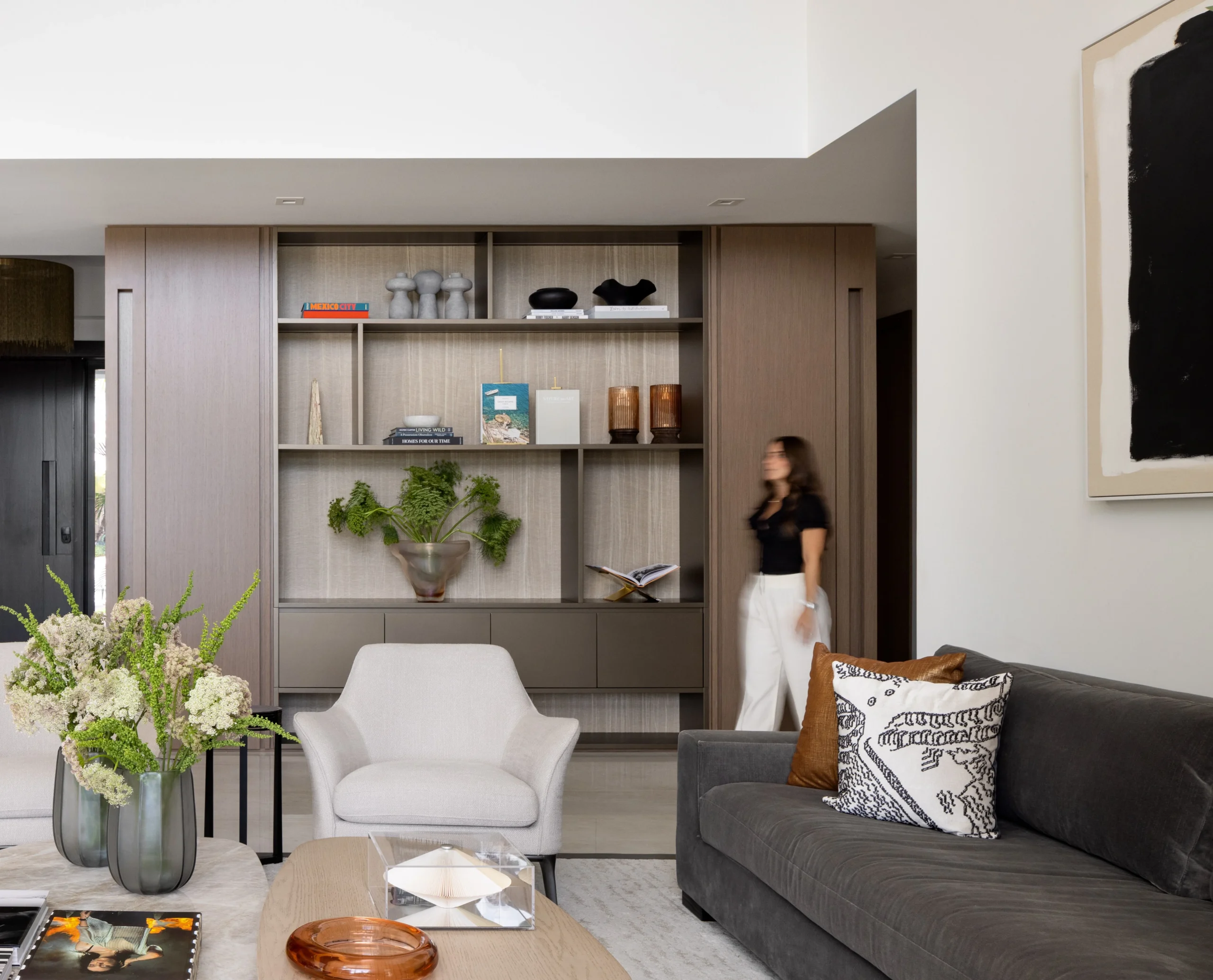 Contemporary living room with custom shelving wall, soft neutral seating and curated decor