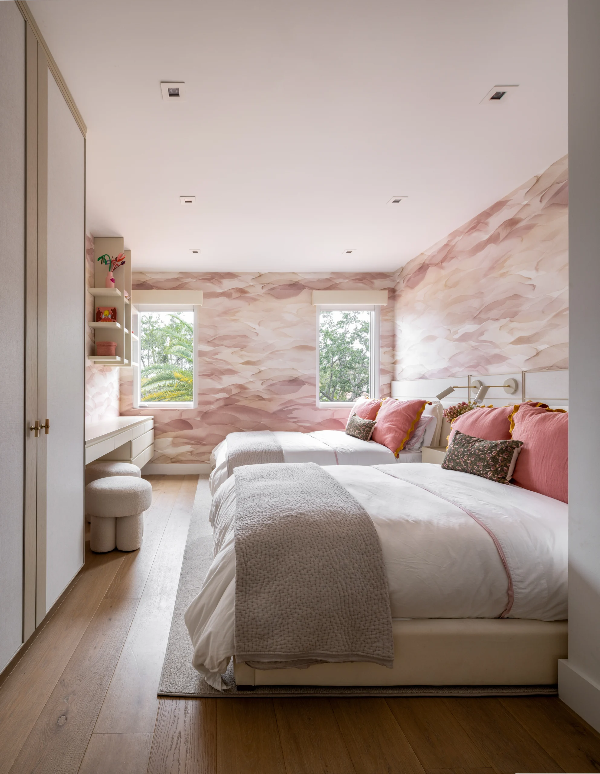 Shared girls' bedroom with twin beds, blush mural wallpaper and built-in vanity desk