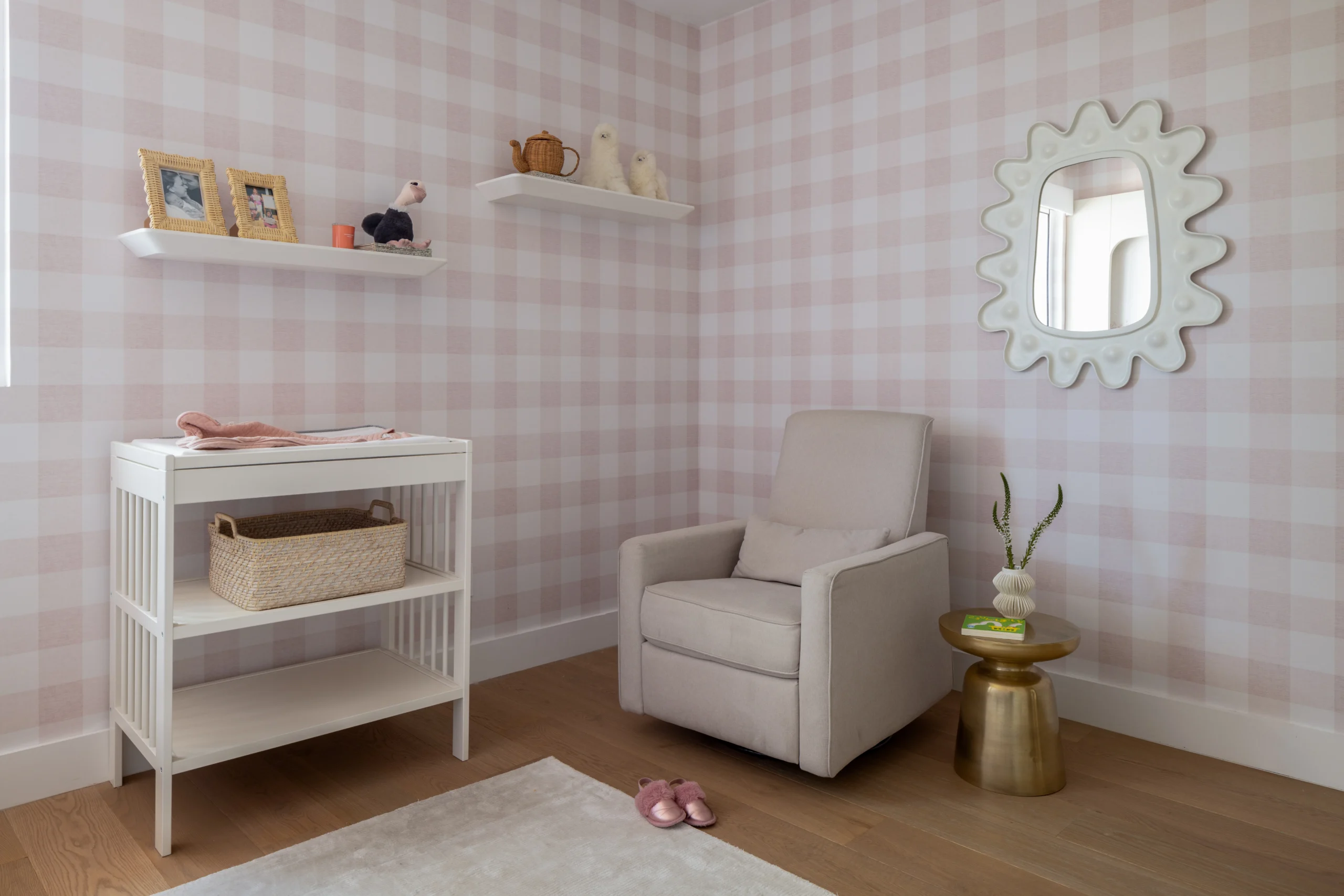 Nursery corner with glider chair, changing table and soft pink gingham wallpaper