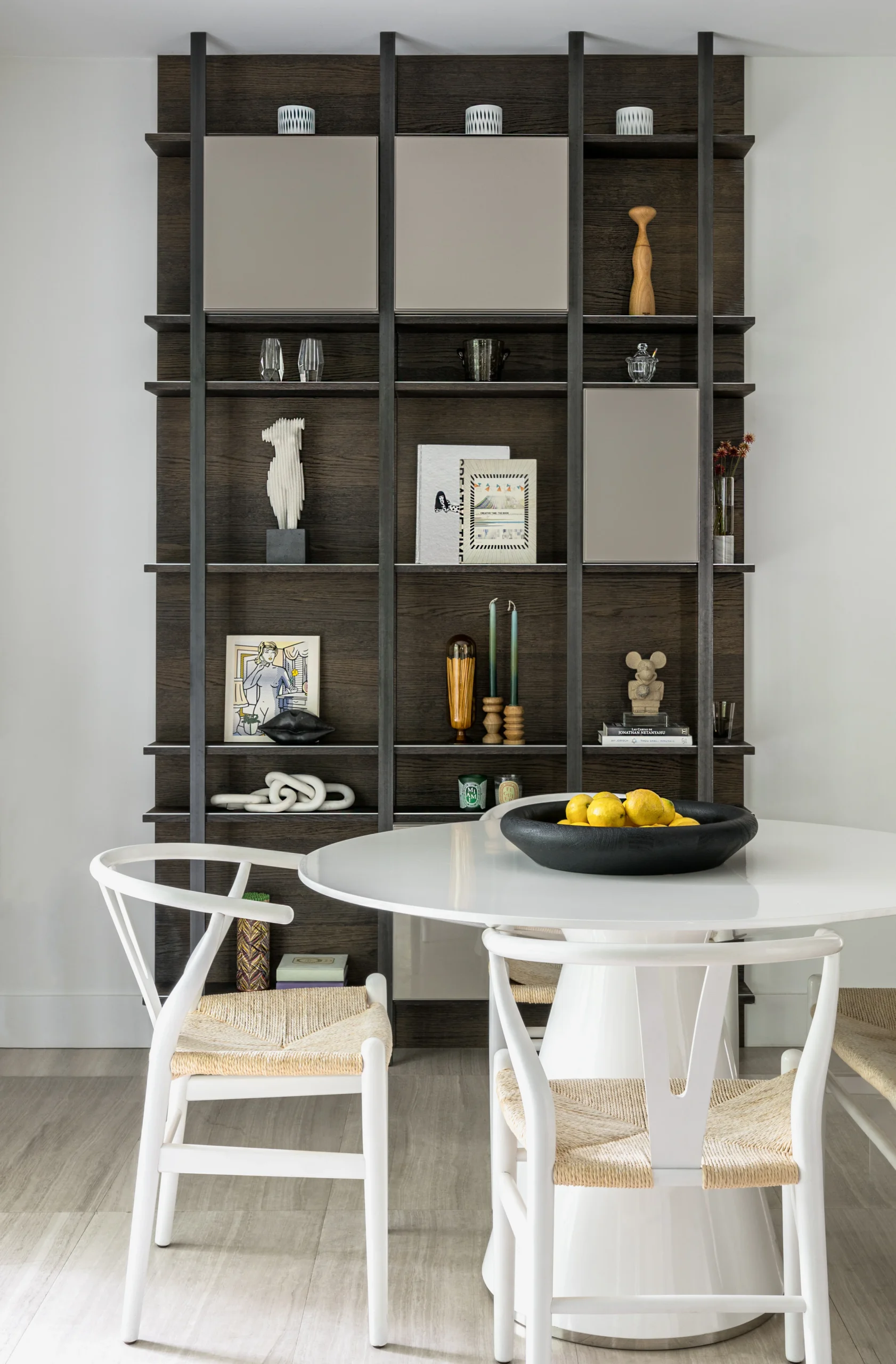 Custom dark oak shelving with round dining table and woven dining chairs in a contemporary residence