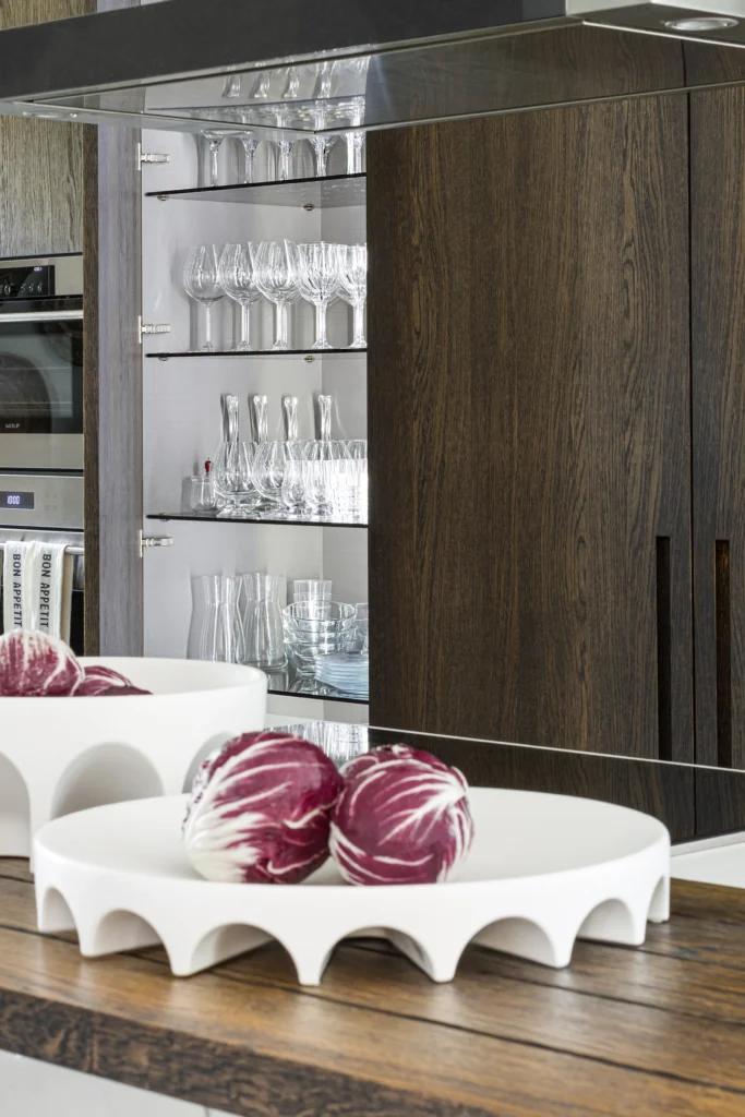 Integrated glassware display cabinet within dark oak kitchen millwork and marble island detail